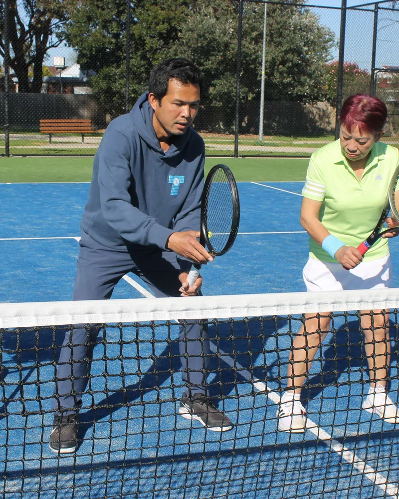 Coach Tuan Nguyen giving an adult private lesson at the net.