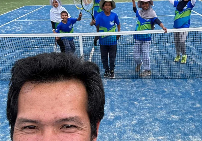 A coach with Hot Shots juniors at the net in blue kit.